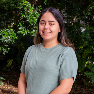Portrait of Ginie Hofmann, Assistant Director of Undergraduate Admissions at the University of Miami, smiling and wearing a white blazer against a blue background.